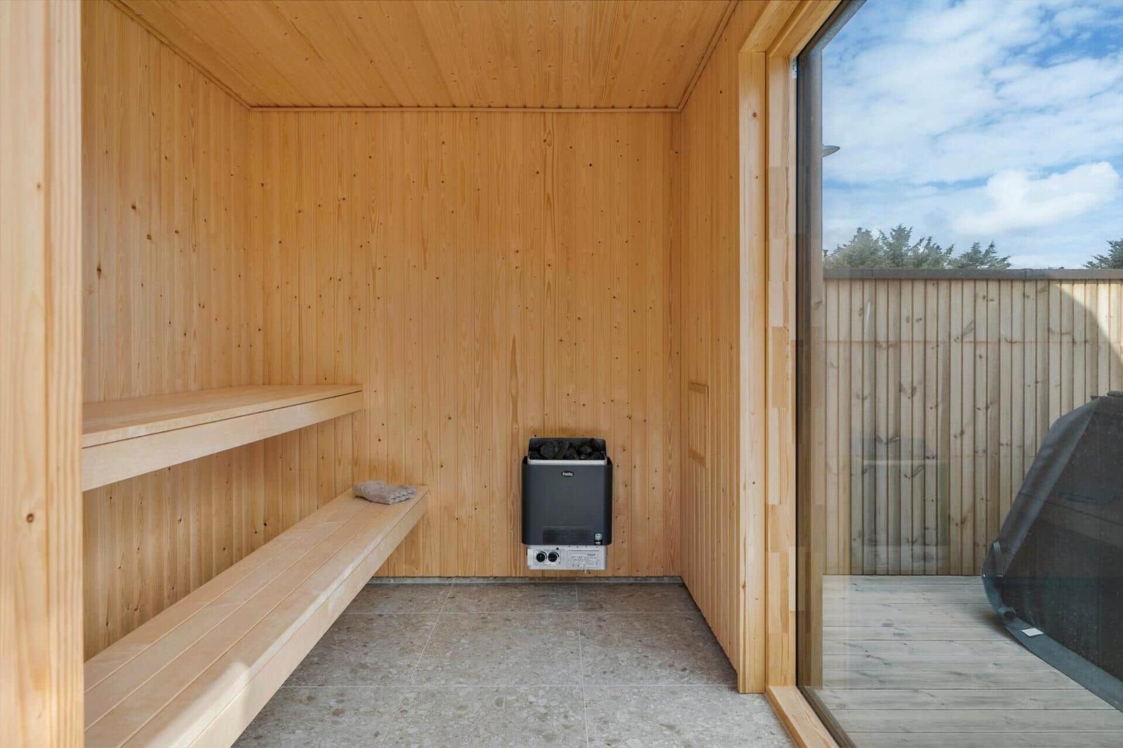 Sauna mit Holzwand, Sitzbank und Heizgerät. Durchgang zu Terrasse mit Holzgeländer.