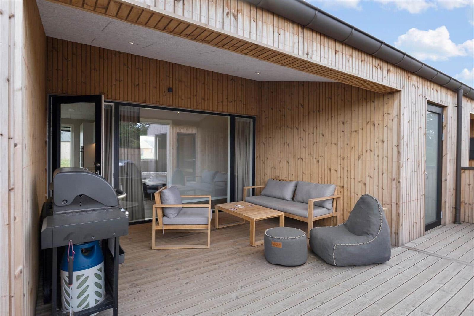 Terrasse mit Sitzgruppe, Grill und Holzwand. Durchgangstür zur Inneneinrichtung.