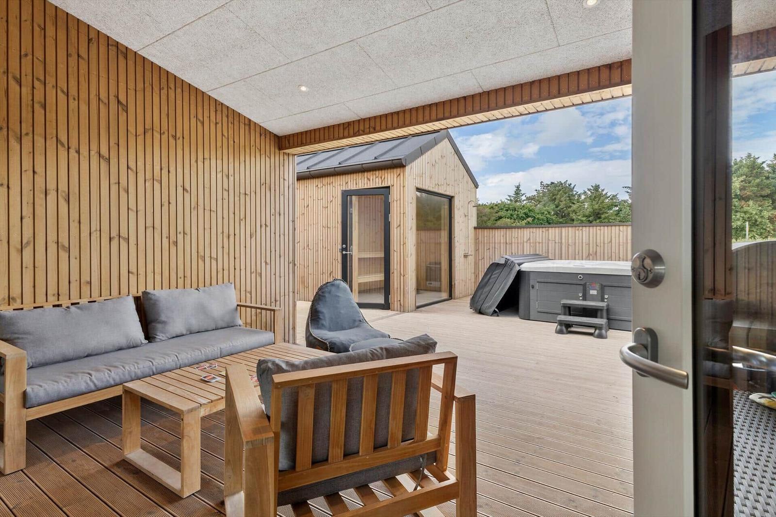 Terrasse mit Sitzgelegenheiten und Sauna. Hintergrund: Whirlpool und Wald.