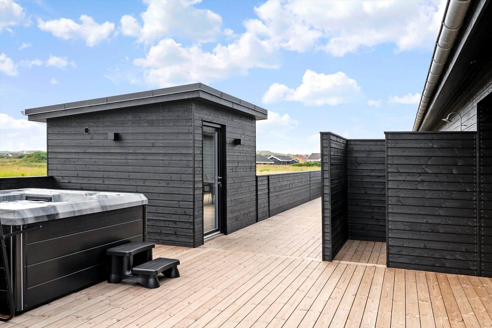 Terrasse mit Whirlpool, schwarzer Holzbarriere und Blick auf die Landschaft.