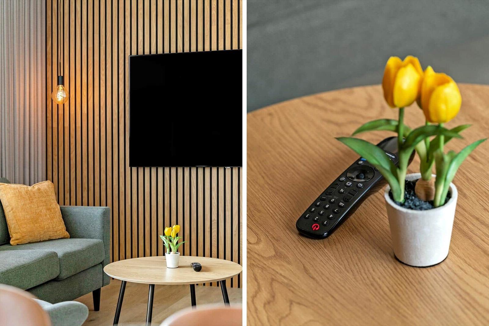 Ein Wohnzimmer mit Sofa, Fernseher und Tisch mit Tulpen. Fernbedienung auf Tisch.