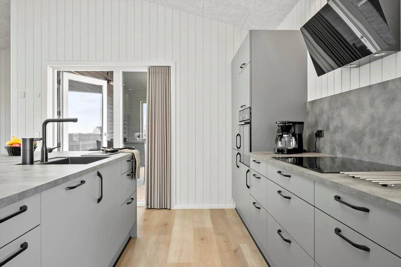 Moderne Küche mit grauen Schränken, Holzboden und Blick auf Balkon.