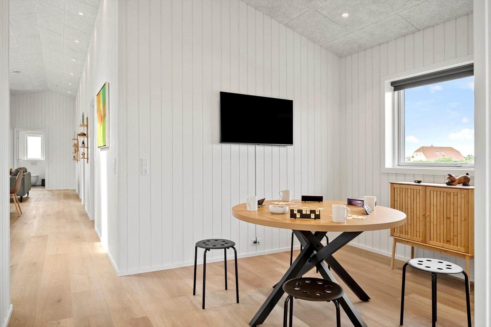 Esszimmer mit runden Tisch, Stühlen und Fernseher an der Wand. Fenster mit Blick auf Dach.