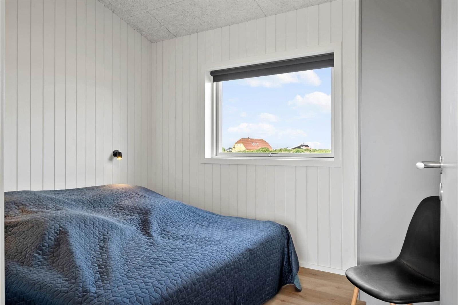 Schlafzimmer mit Bett, Fenster und Stuhl. Blick auf Dach und Himmel.