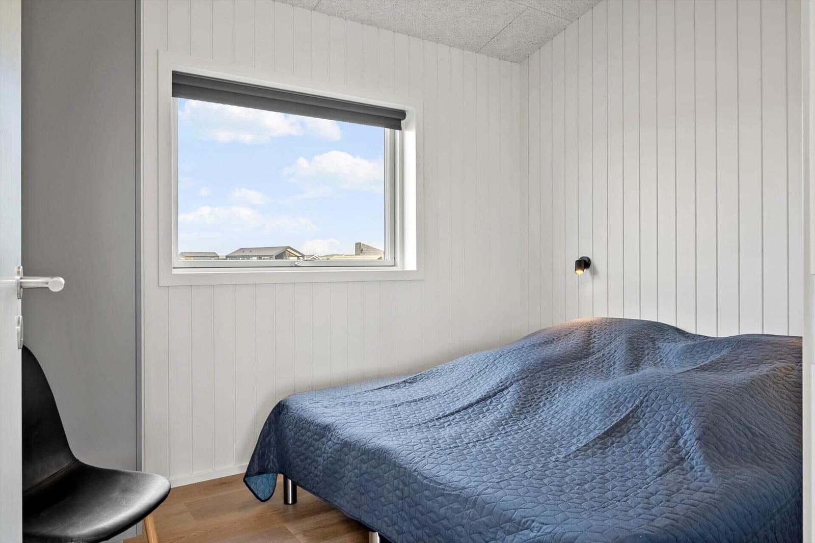 Schlafzimmer mit Bett, Fenster und Stuhl.