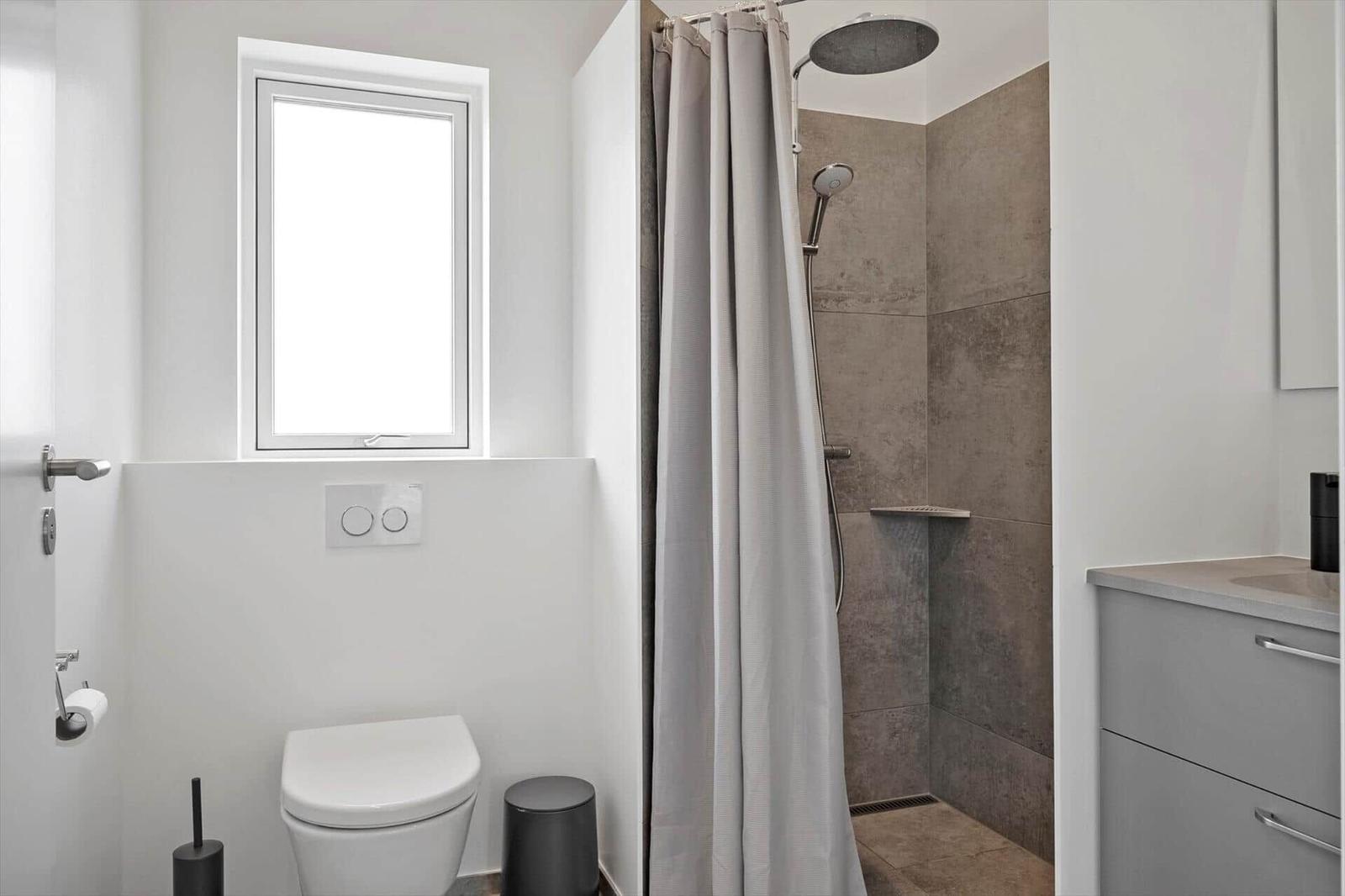 Badezimmer mit Dusche, Toilette und Waschbecken. Fenster sorgt für Tageslicht.