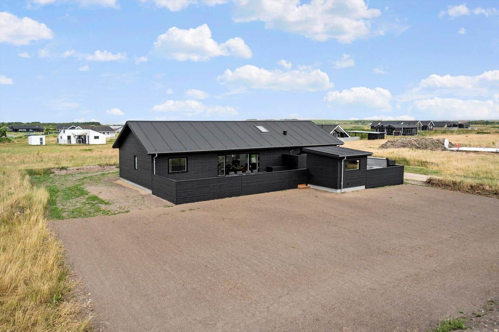 Moderne schwarze Villa mit großem Dachfenster und Terrasse in ländlicher Umgebung.