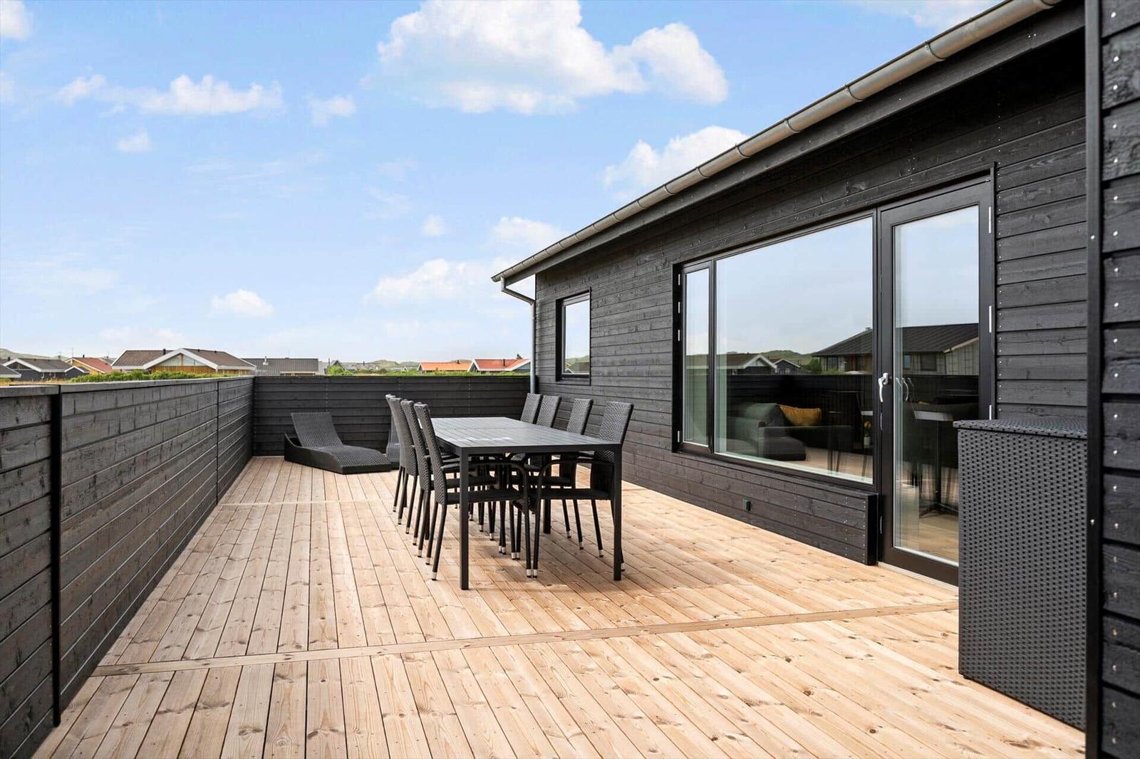 Terrasse mit Tisch und Stühlen, Holzboden und schwarzer Holzwand.