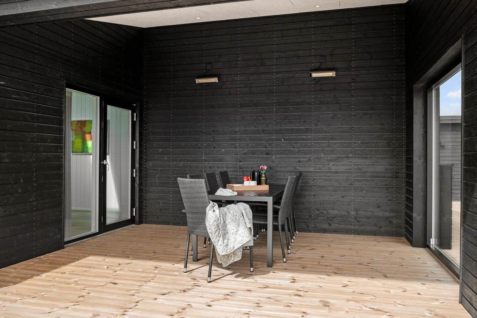 Außenbereich mit Esstisch, Stühlen und Holzboden. Schwarze Holzwände und Glastüren.