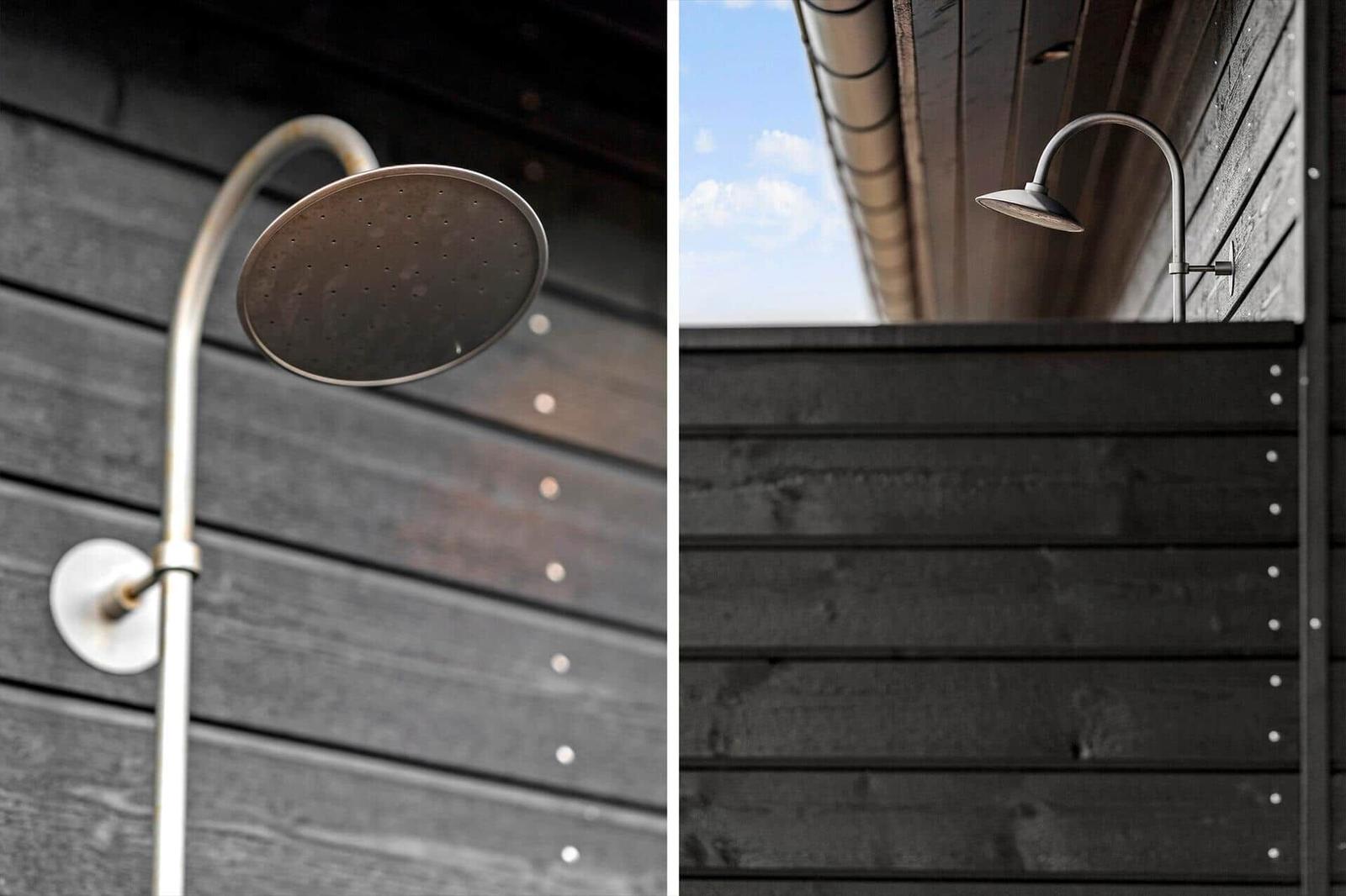 Außendusche mit Duschbrause an dunkler Holzwand. Blick auf Himmel und Dachrinne.
