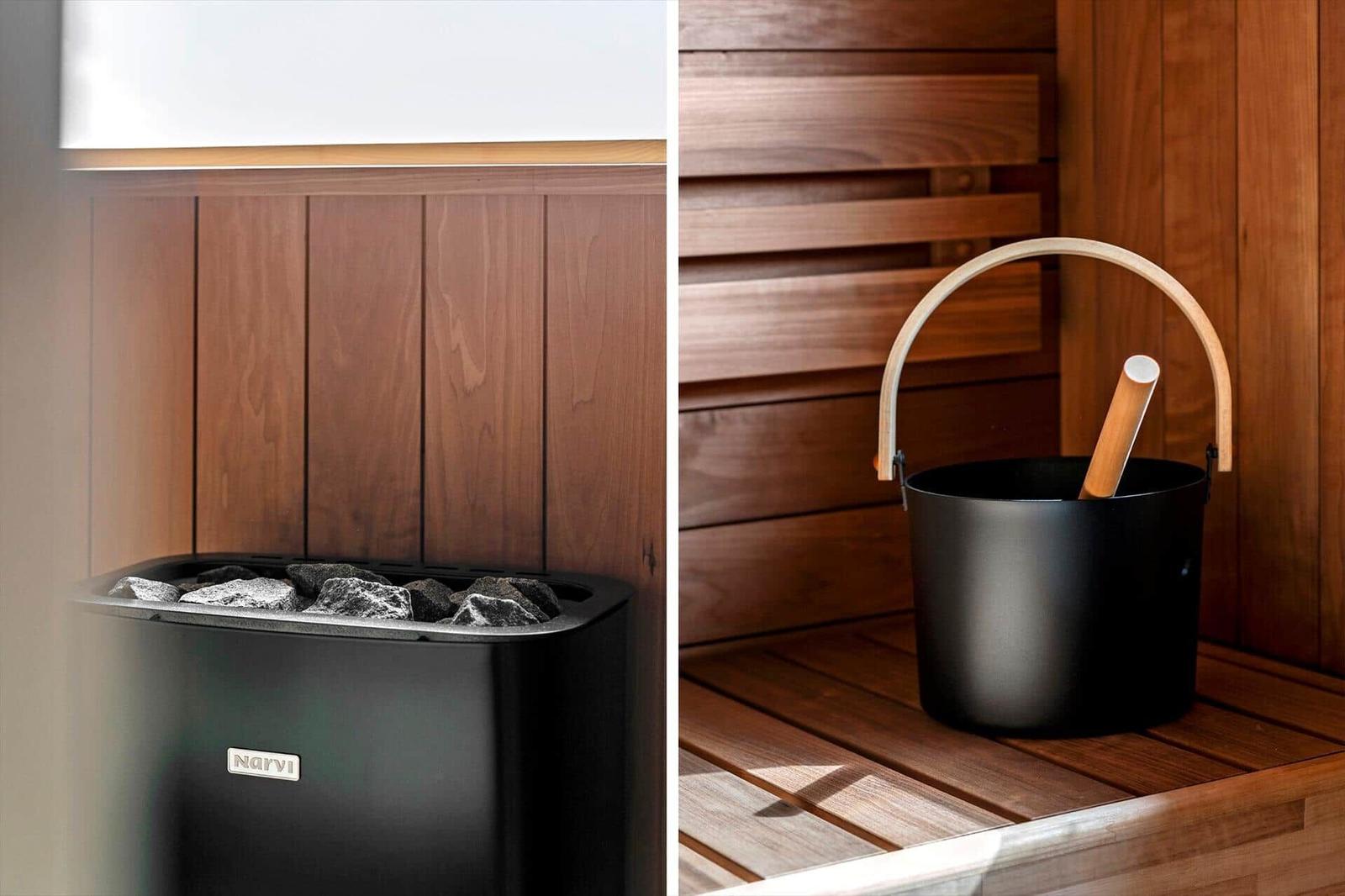 Sauna mit Holzwand und schwarzer Eimer mit Besen. Links: Heizung mit Steinen.