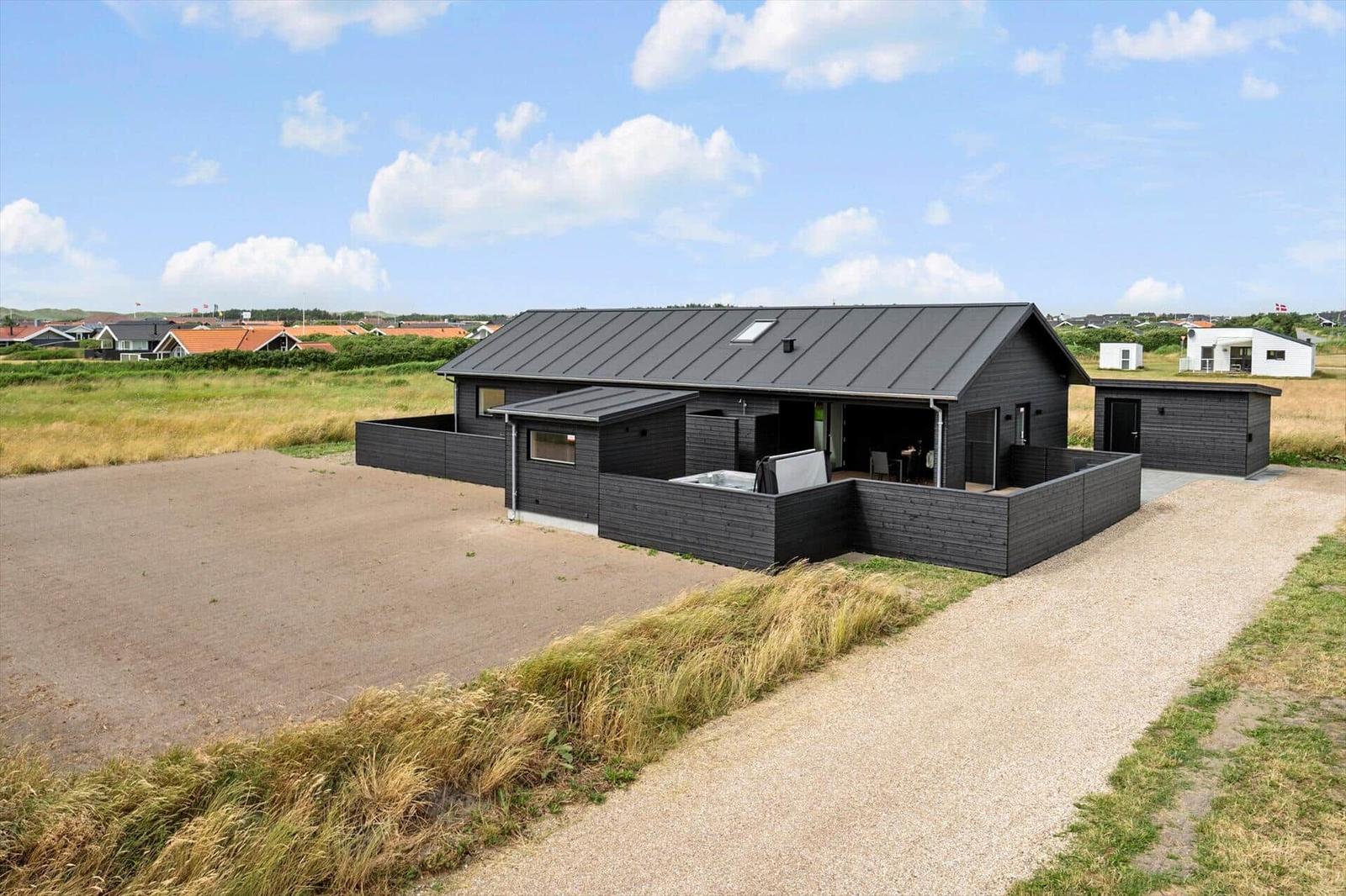Moderne Villa mit Terrasse und Garten. Dunkle Holzfassade und flachem Dach. Grasland im Hintergrund.