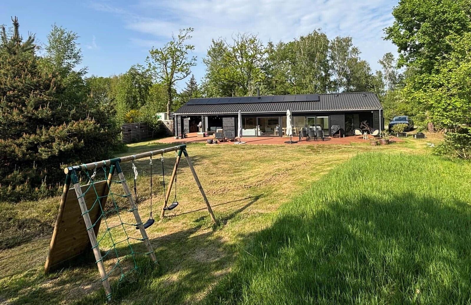 Modernes Haus mit Terrasse, Spielplatz und grünem Garten in Waldnähe.