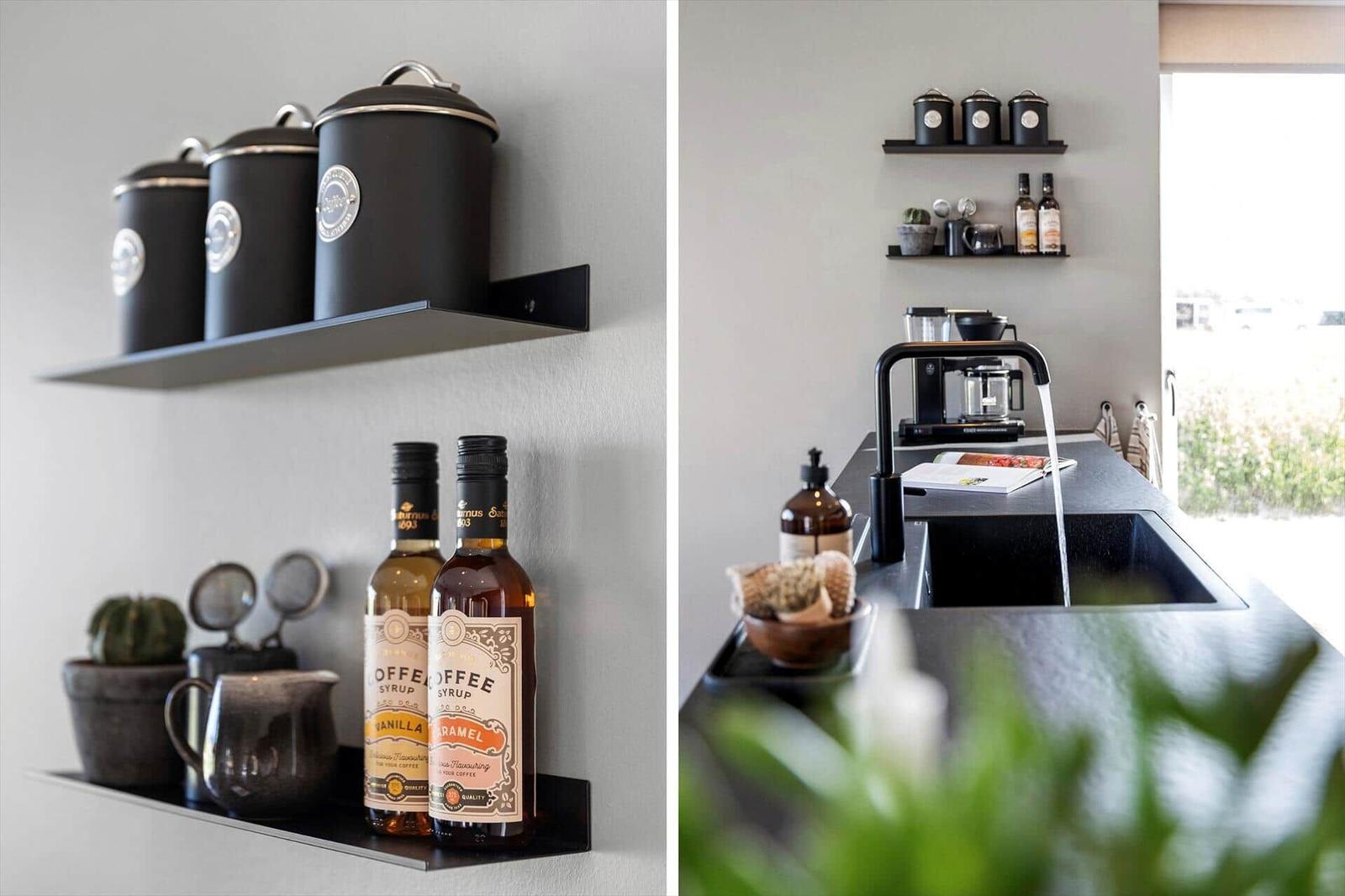 Küche mit schwarzen Regalen, Kaffeemaschine und Flaschen mit Sirup.
