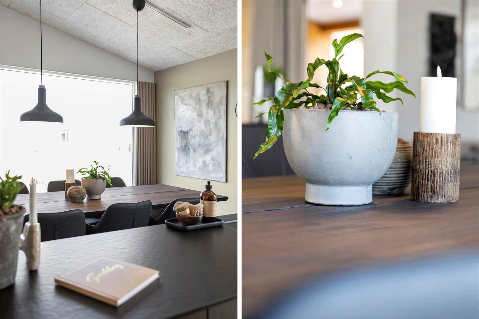 Esstisch mit Pflanzen, Kerzen und Dekor auf dunklem Holz. Hängelampen und Wandbild im Hintergrund.