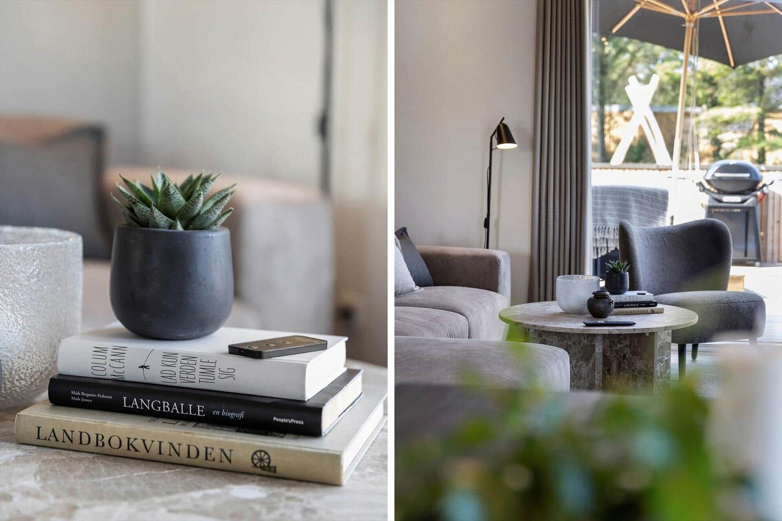 Tisch mit Büchern und Pflanze. Wohnbereich mit Sofa, Sessel und Blick auf Terrasse.