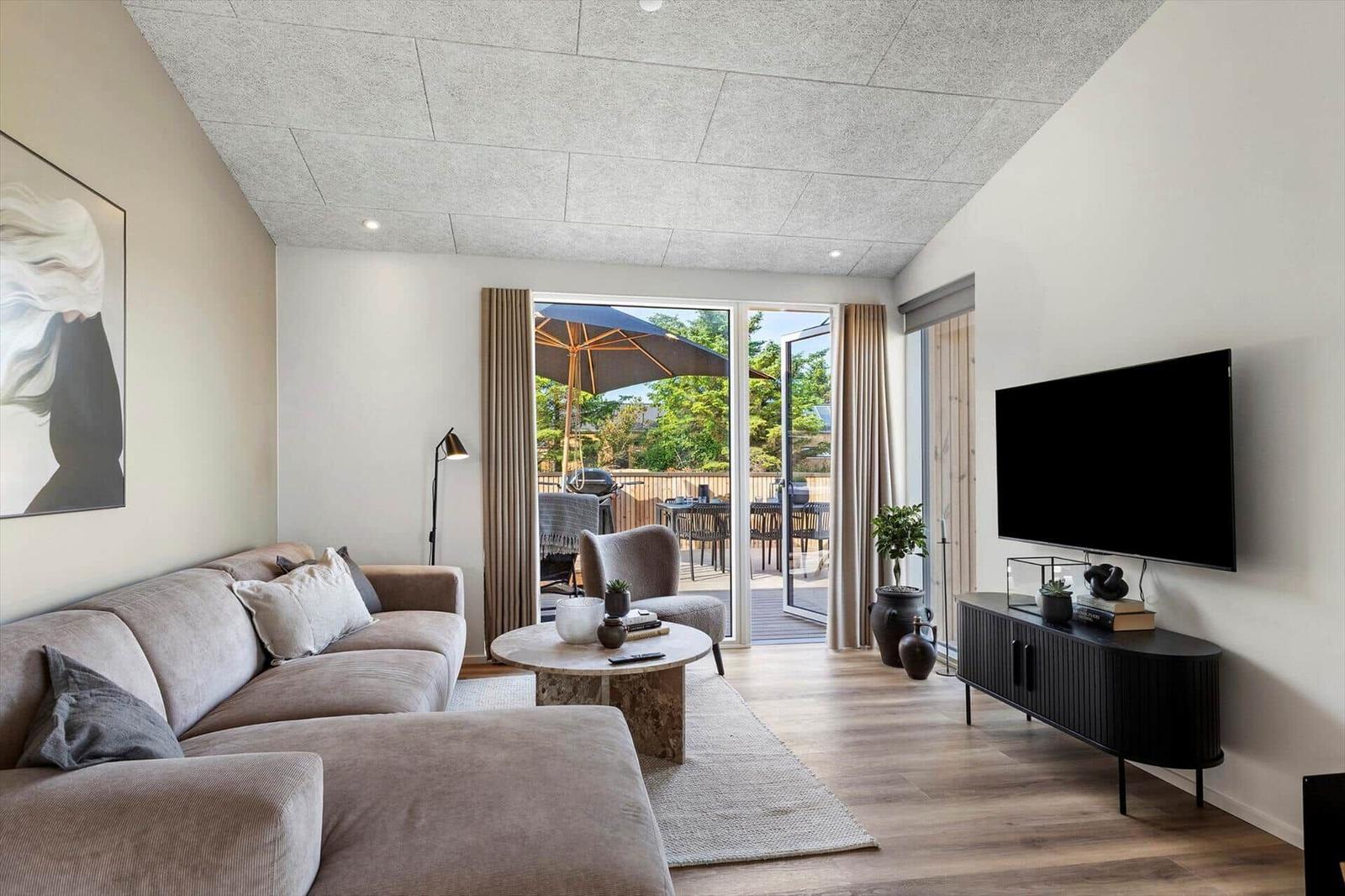 Wohnzimmer mit Sofa, TV und Terrasse mit Sonnenschirm.