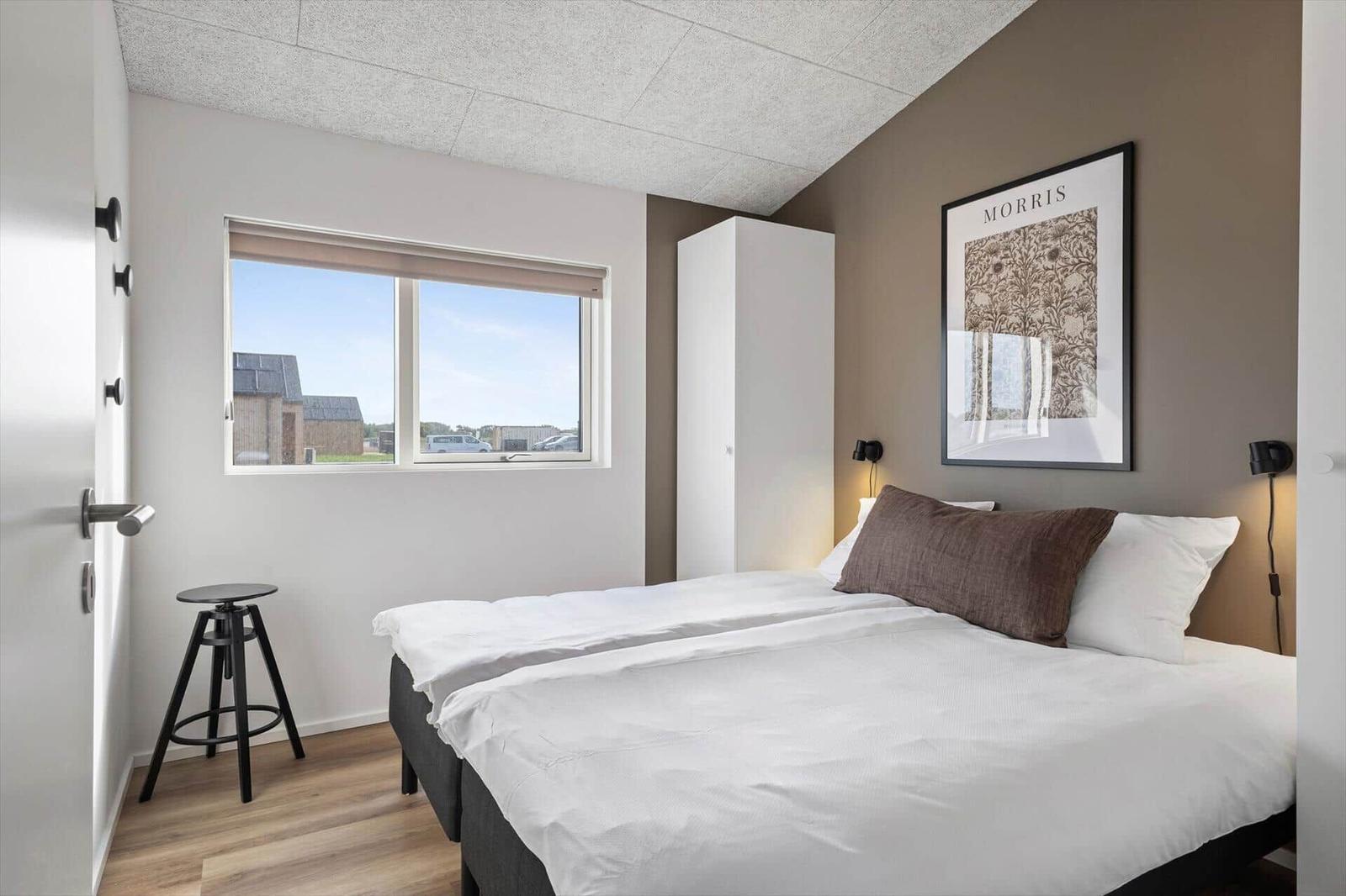 Schlafzimmer mit Doppelbett, Fenster und Wandbild. Holzfußboden und weißer Kleiderschrank.