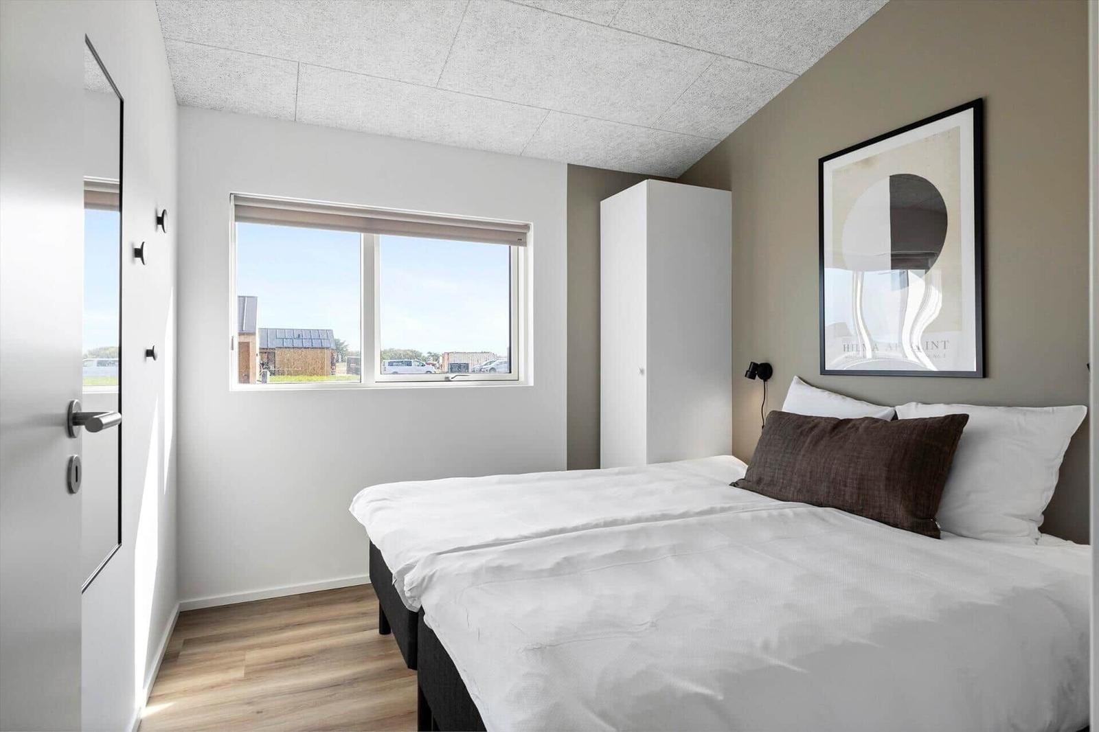 Schlafzimmer mit Bett, Fenster und Wandbild. Holzfußboden und weißer Kleiderschrank.