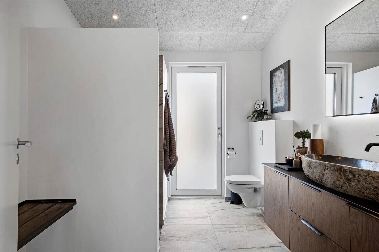 Moderne Badewanne mit Holzschrank und Waschbecken. Toilette und Dusche sind sichtbar.