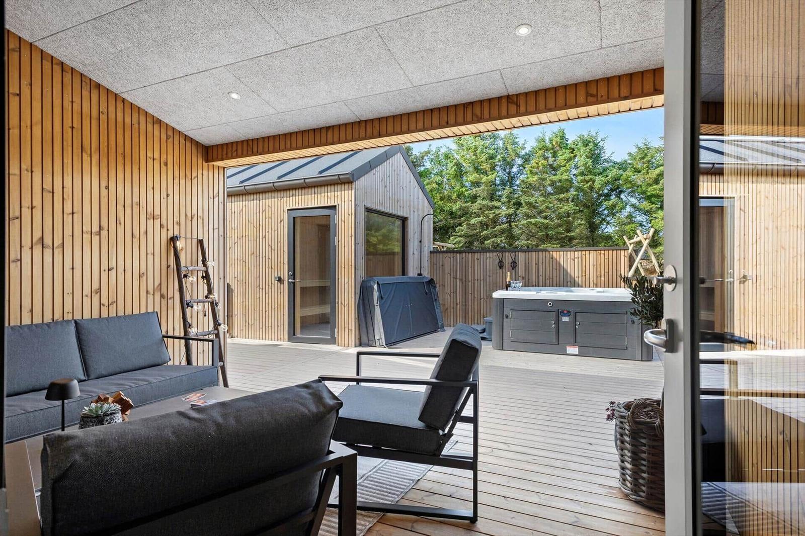 Terrasse mit Sitzgruppe, Whirlpool und Holzhaus im Hintergrund.