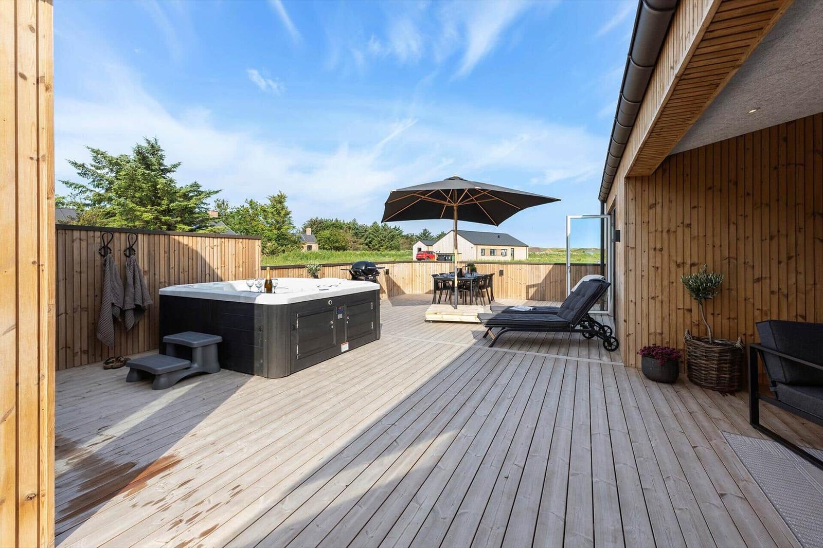 Terrasse mit Whirlpool, Sonnenliege und Tisch unter Sonnenschirm.