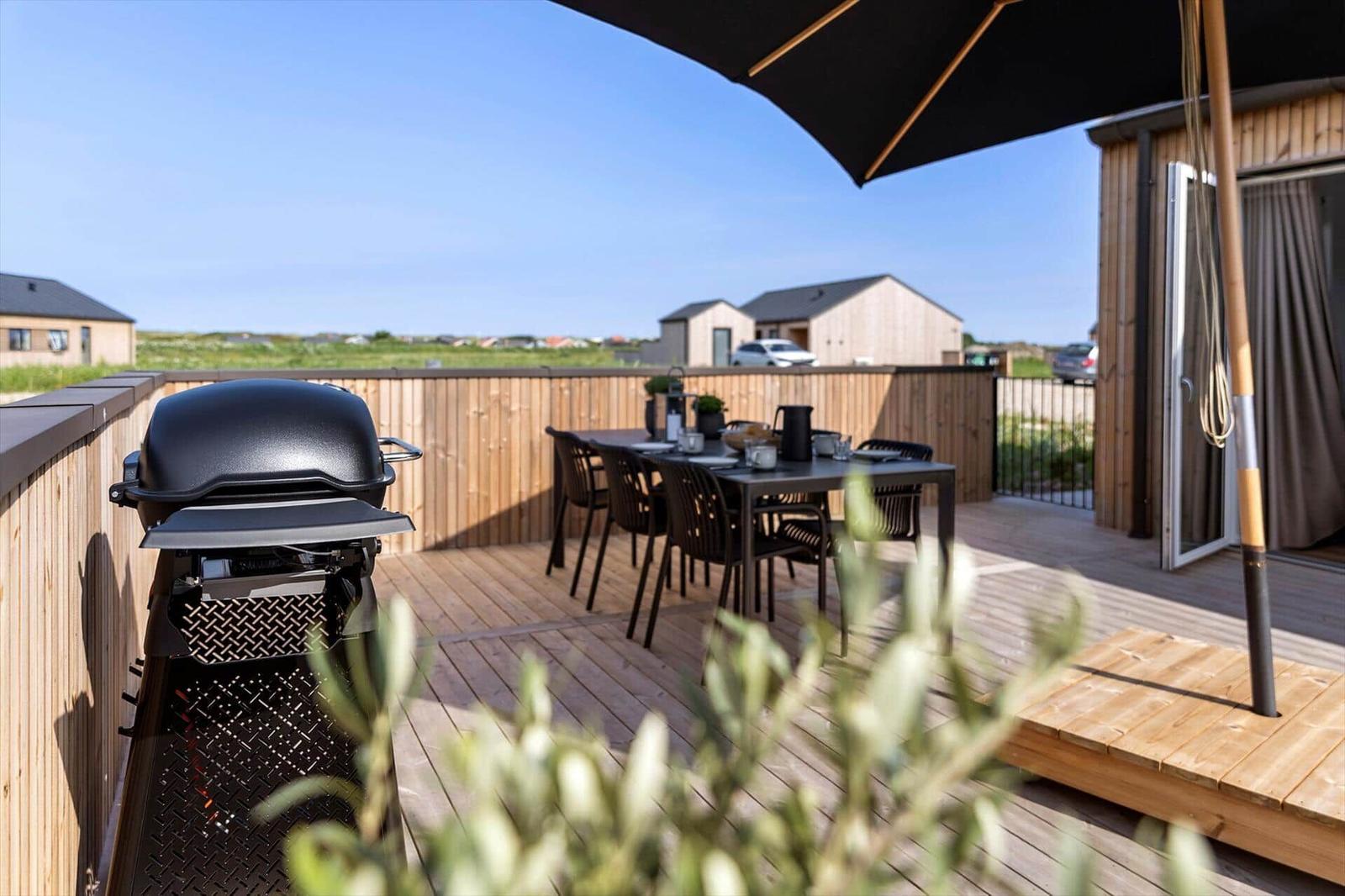 Terrasse mit Grill, Tisch und Stühlen unter einem Sonnenschirm.