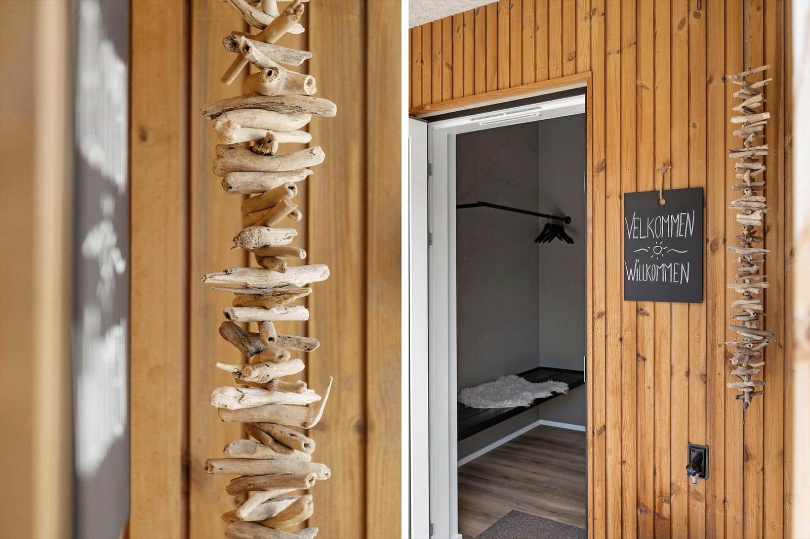 Eingangsbereich mit Holzwand und Willkommensschild. Tür führt in einen Kleiderschrank mit Kleiderständer.