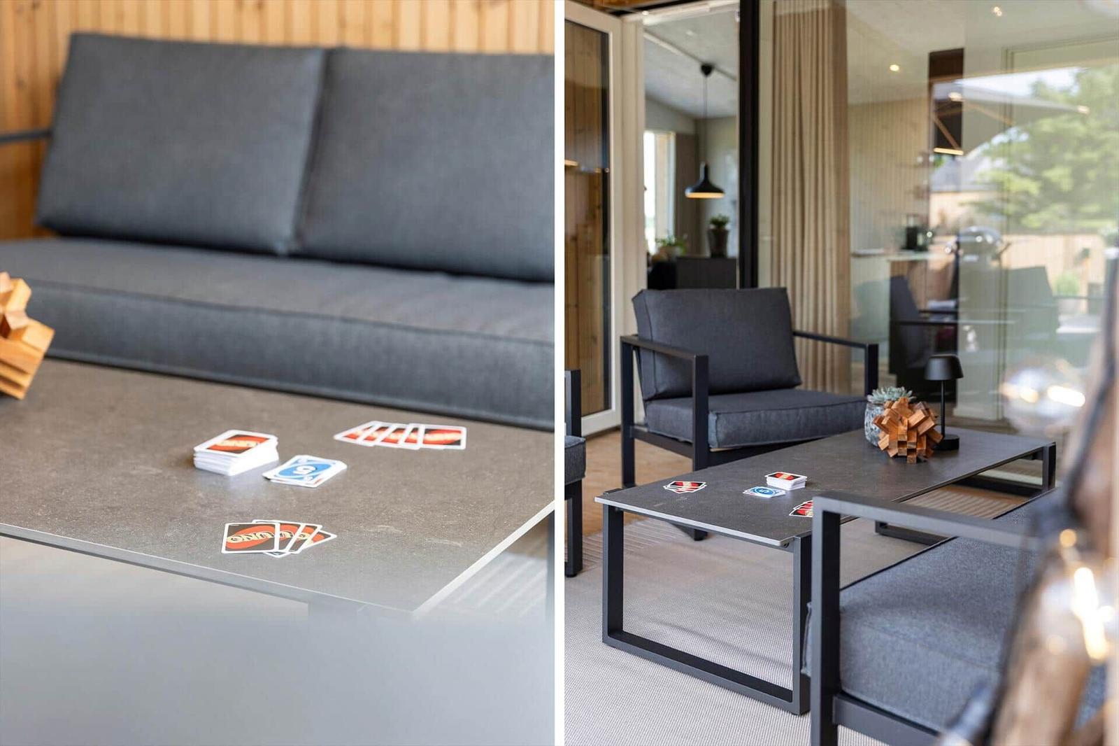 Sofa und Sitzgruppe mit Tisch und Spielkarten. Glaswand trennt Wohn- und Essbereich.
