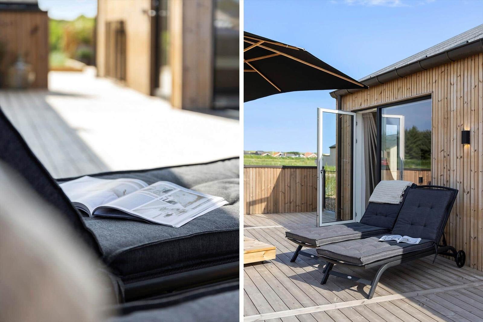 Terrasse mit Liegen und Sonnenschutz. Bücher auf der Auflage. Holzhaus im Hintergrund.