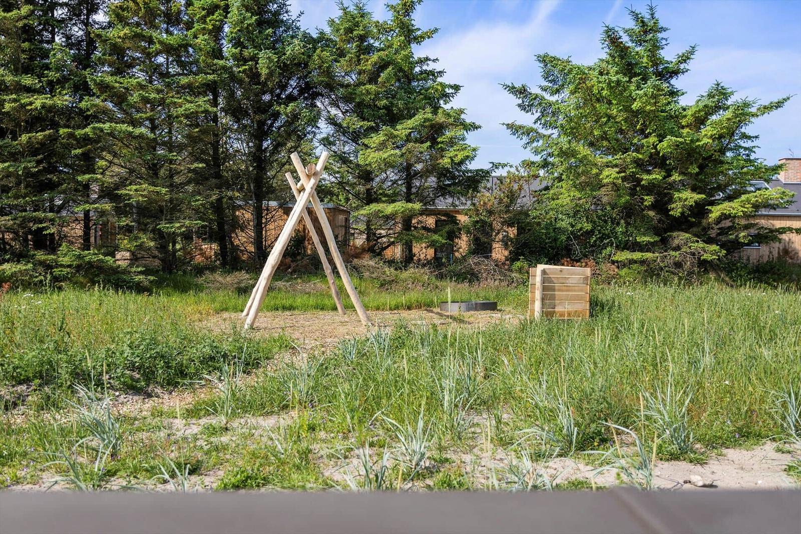 Hinterhof mit Holzkonstruktion, Garten und Bäumen. Im Hintergrund ein Holzhaus.