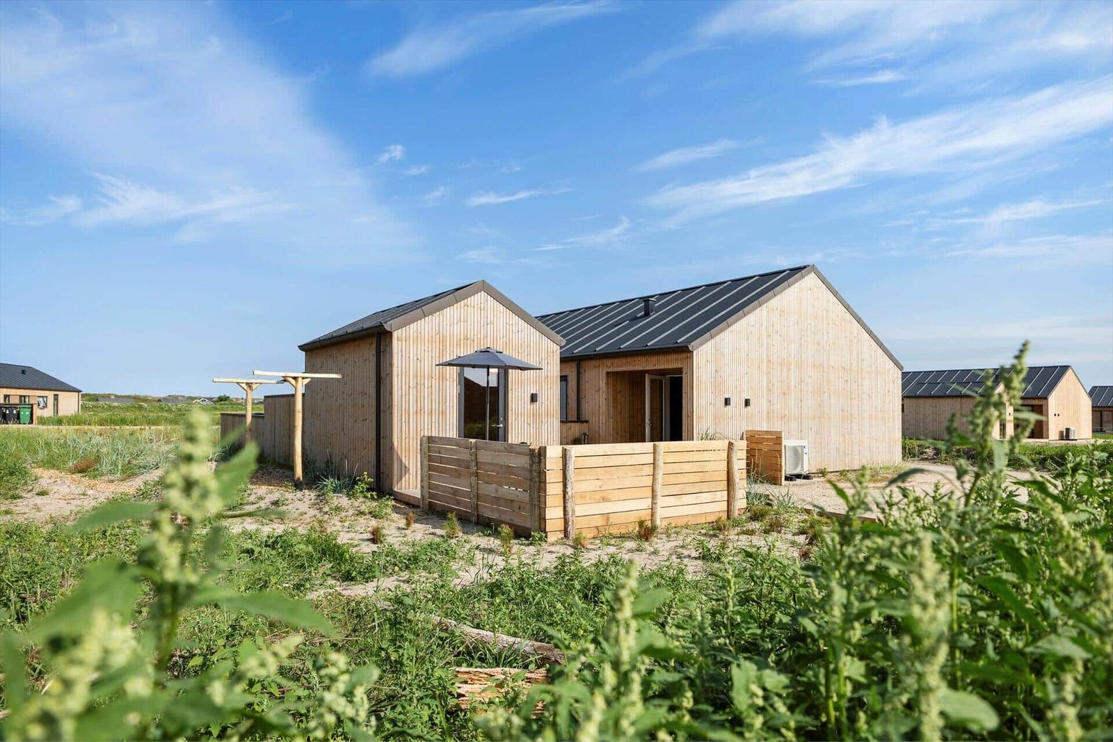 Holzhaus mit Garten und Sonnenschutz unter blauem Himmel.