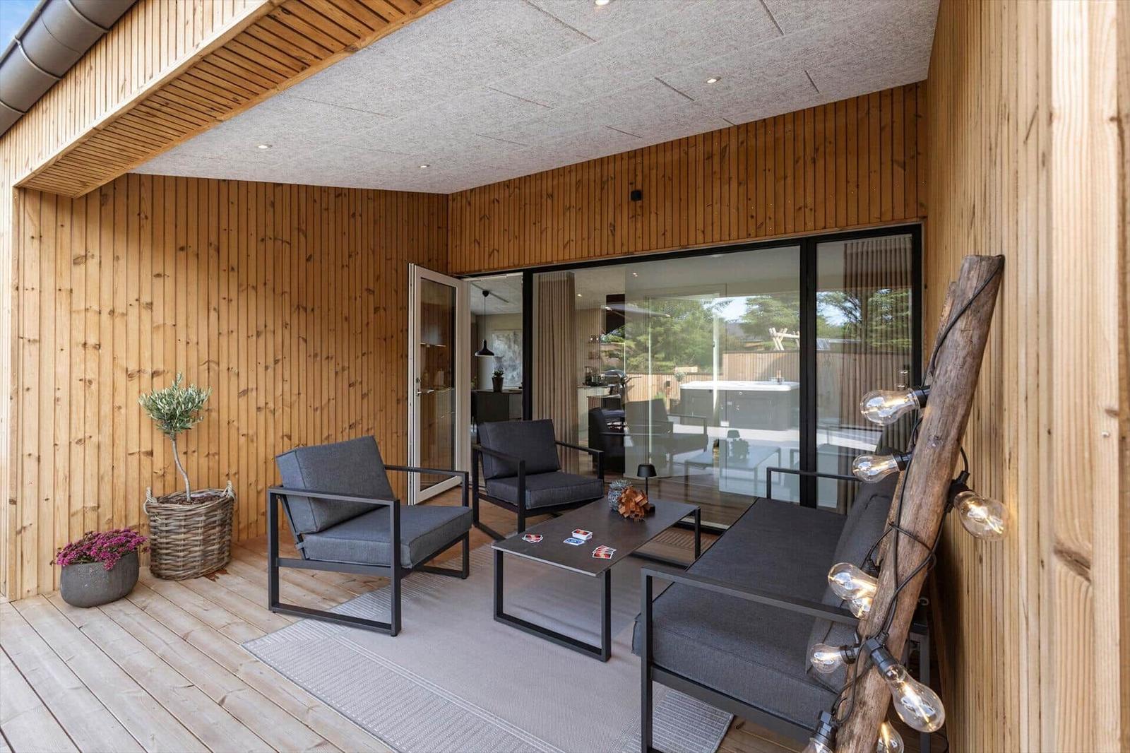 Terrasse mit Sitzgruppe, Pflanzen und Lichterkette an Holzwand.