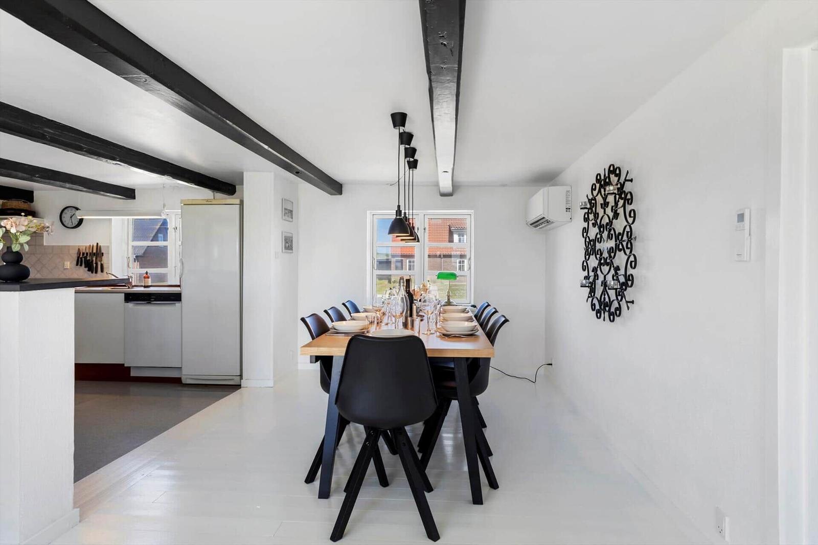 Essbereich mit Tisch und Stühlen, Küche im Hintergrund, schwarze Balken an der Decke.