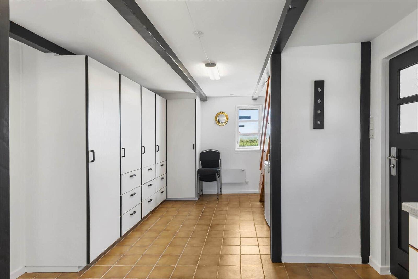 Flur mit weißen Schränken, braunem Fliesenboden und schwarzen Balken an der Decke.
