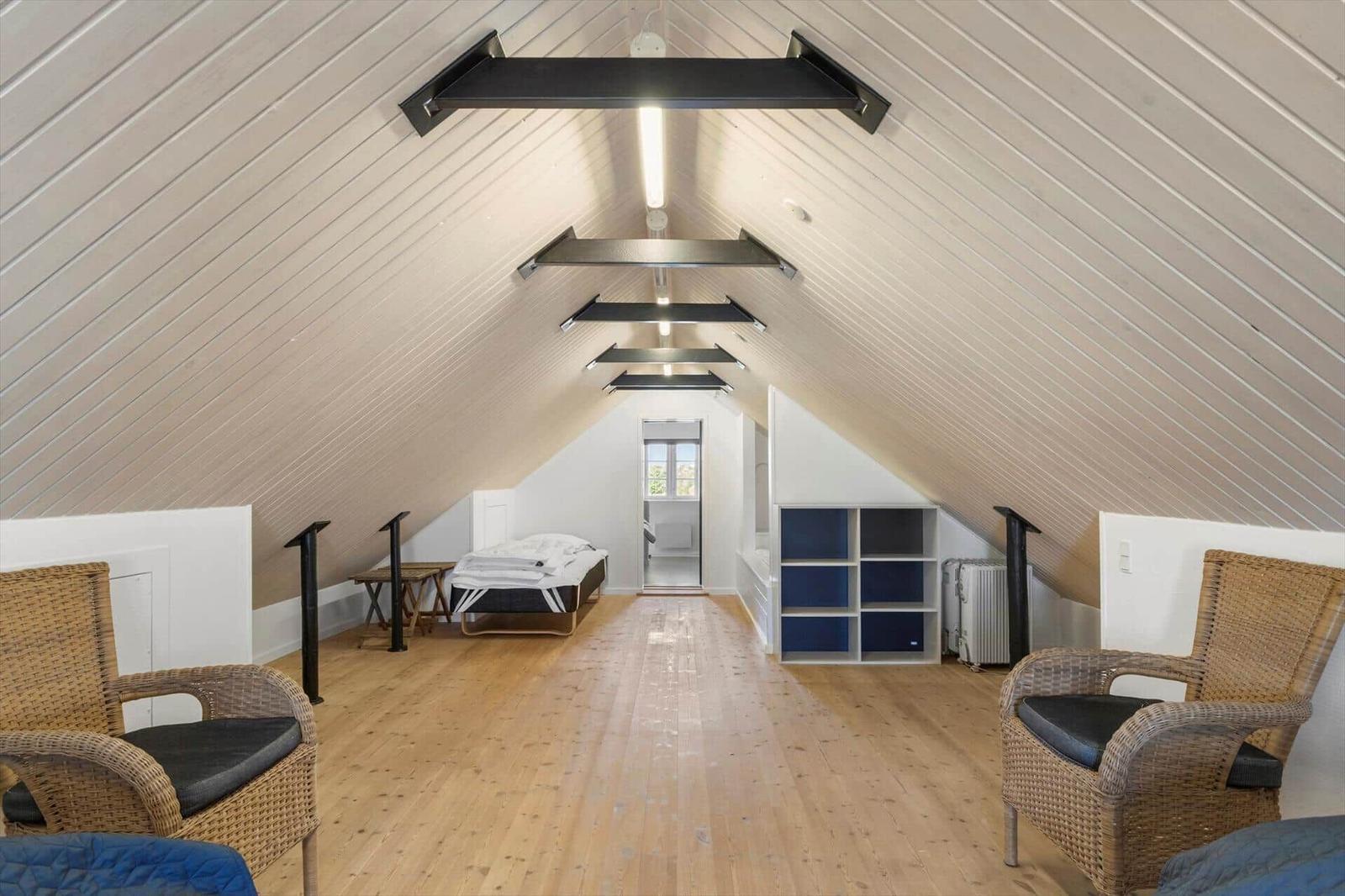 Dachgeschosszimmer mit Holzboden, zwei Stühlen und Bett im Hintergrund.