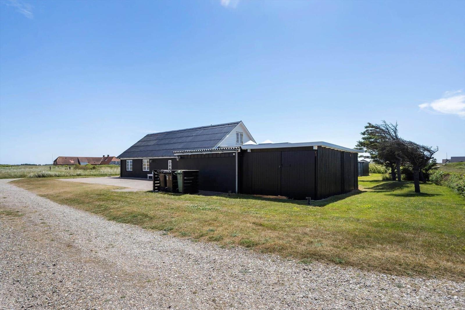 Ein dunkles Haus mit Garage steht auf einem Grünland unter blauem Himmel.