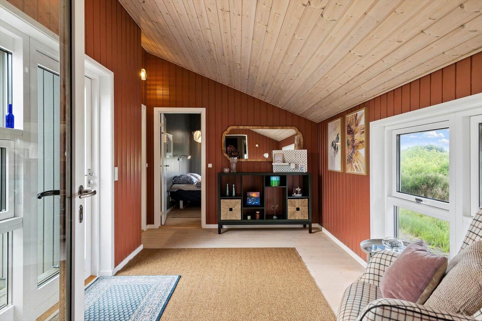 Raum mit Holzdecke, roten Wänden und Fensterblick auf Grünflächen