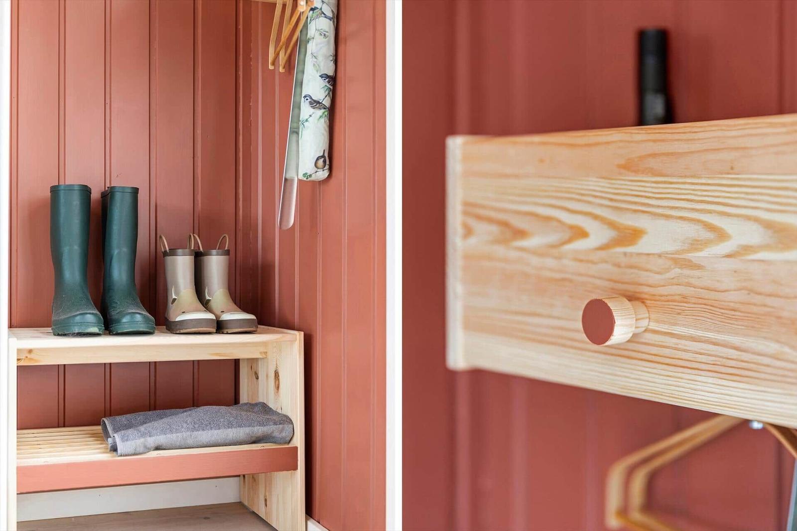 Holzregal mit Gummistiefeln und Handtuch an roter Wand