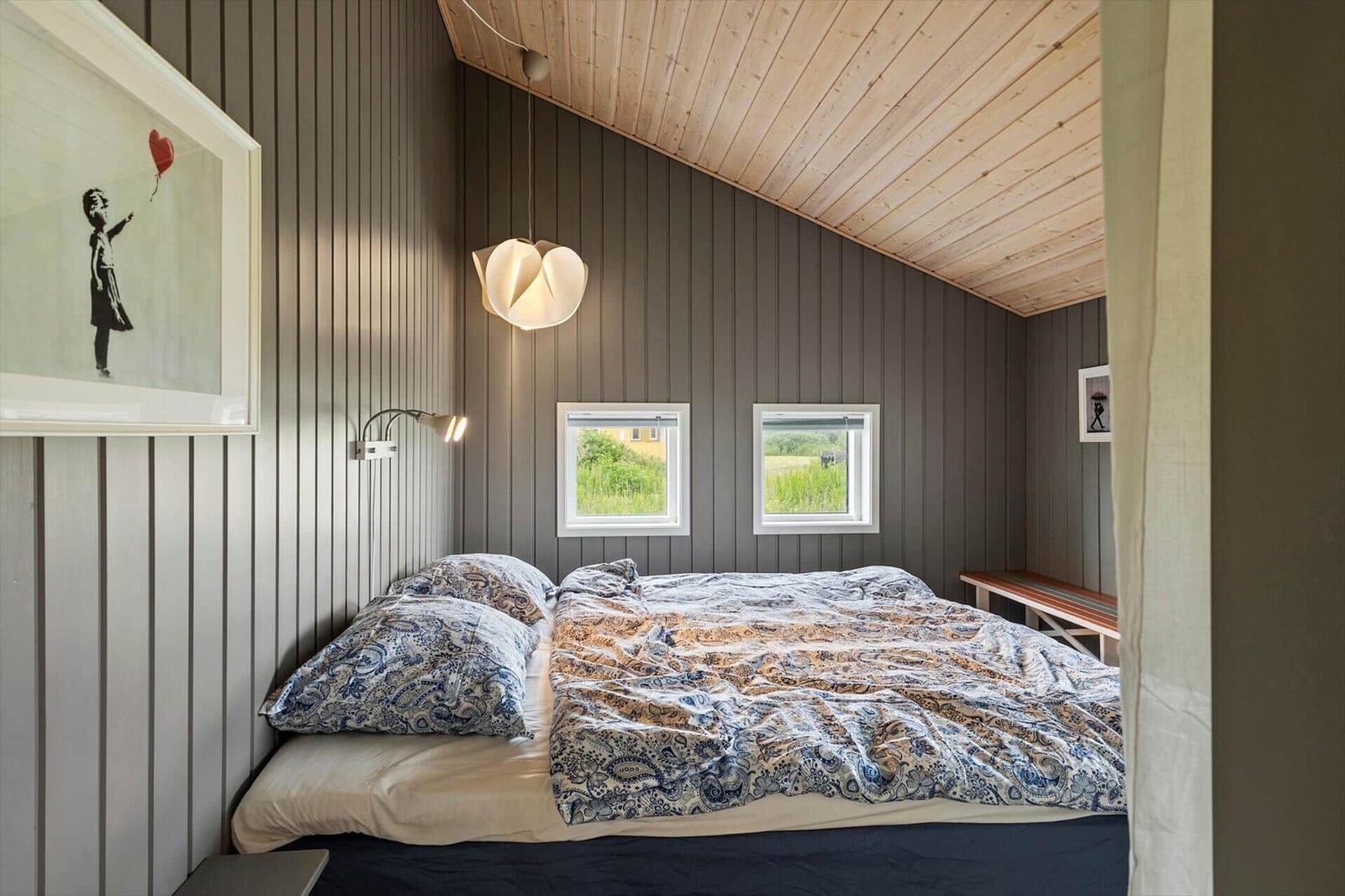 Schlafzimmer mit Bett, zwei Fenstern und Holzdecke.
