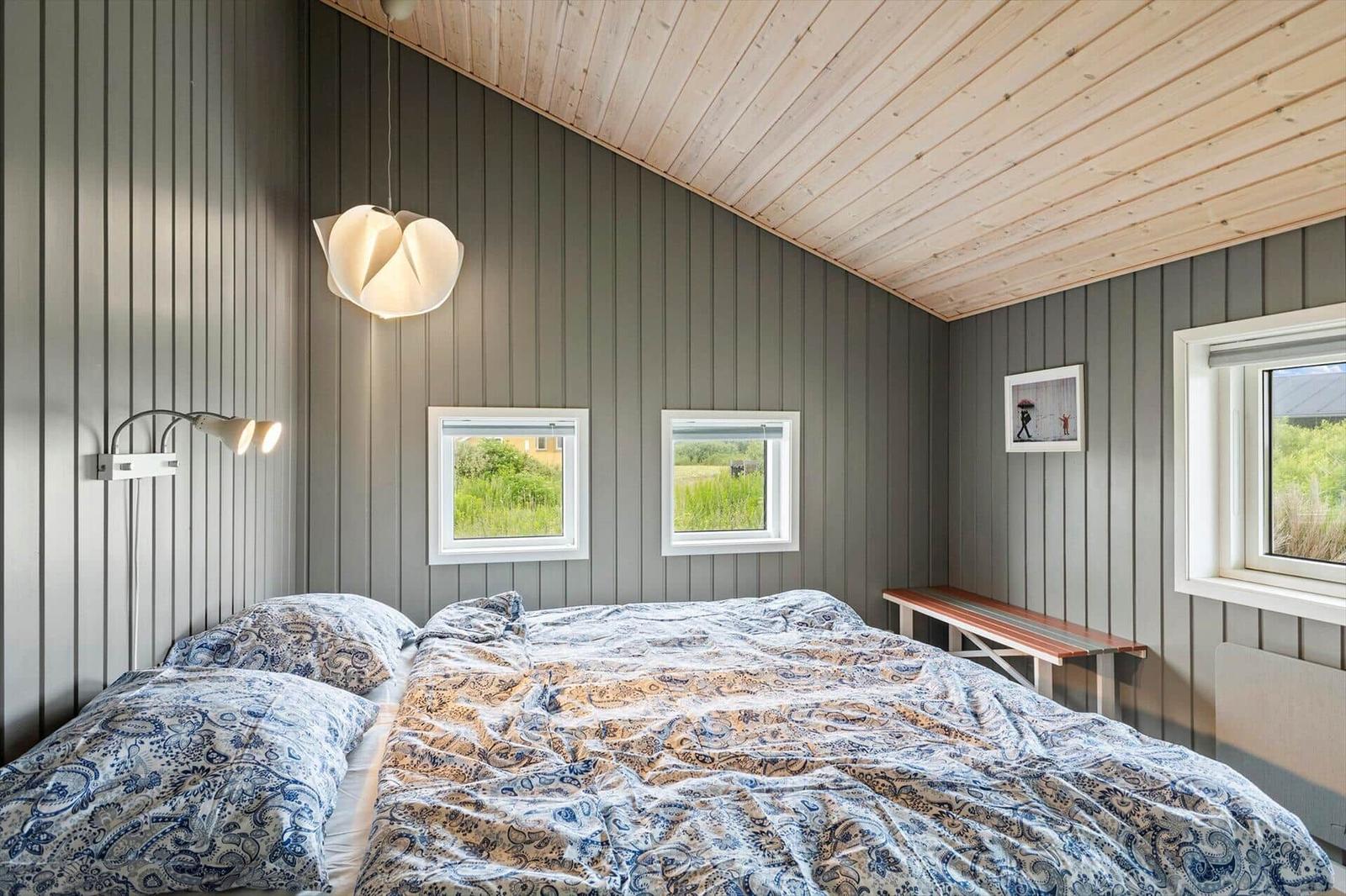 Schlafzimmer mit Bett, Fenstern und Holzdecke.