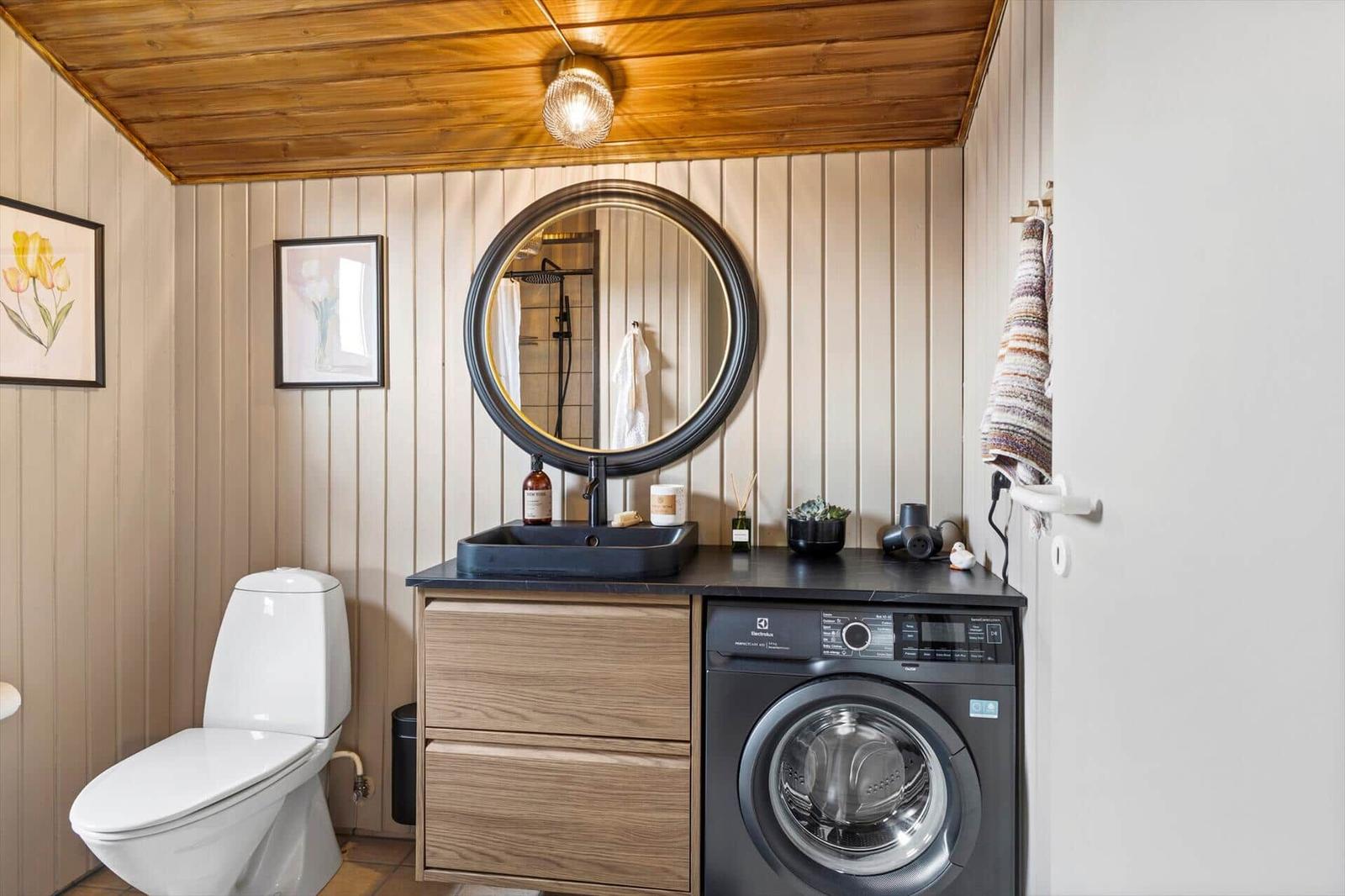 Badezimmer mit Waschmaschine, Spiegel und Toilette.