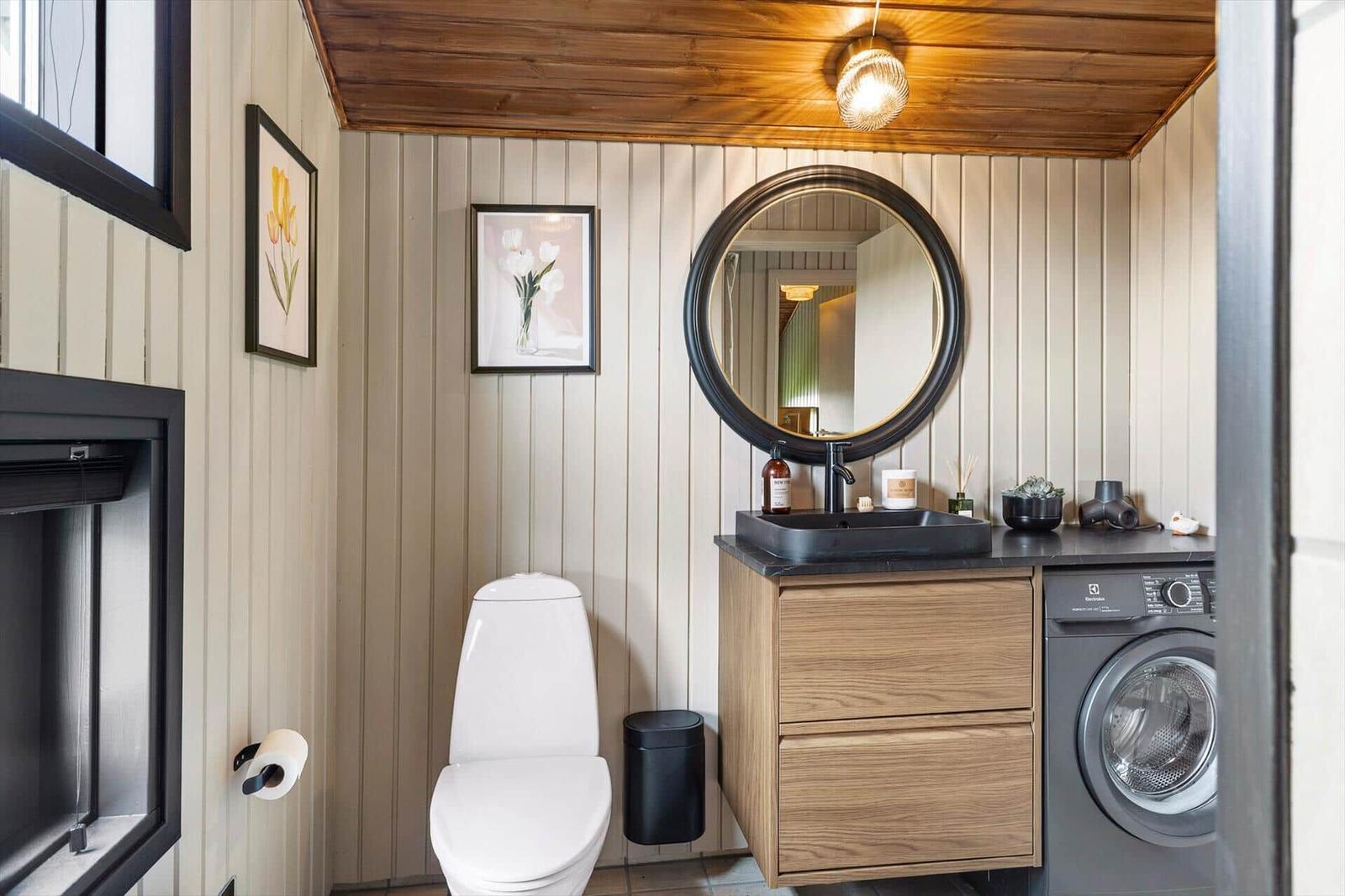 Badezimmer mit Toilette, Waschbecken und Waschmaschine. Holzdecke und vertikale Wandverkleidung.