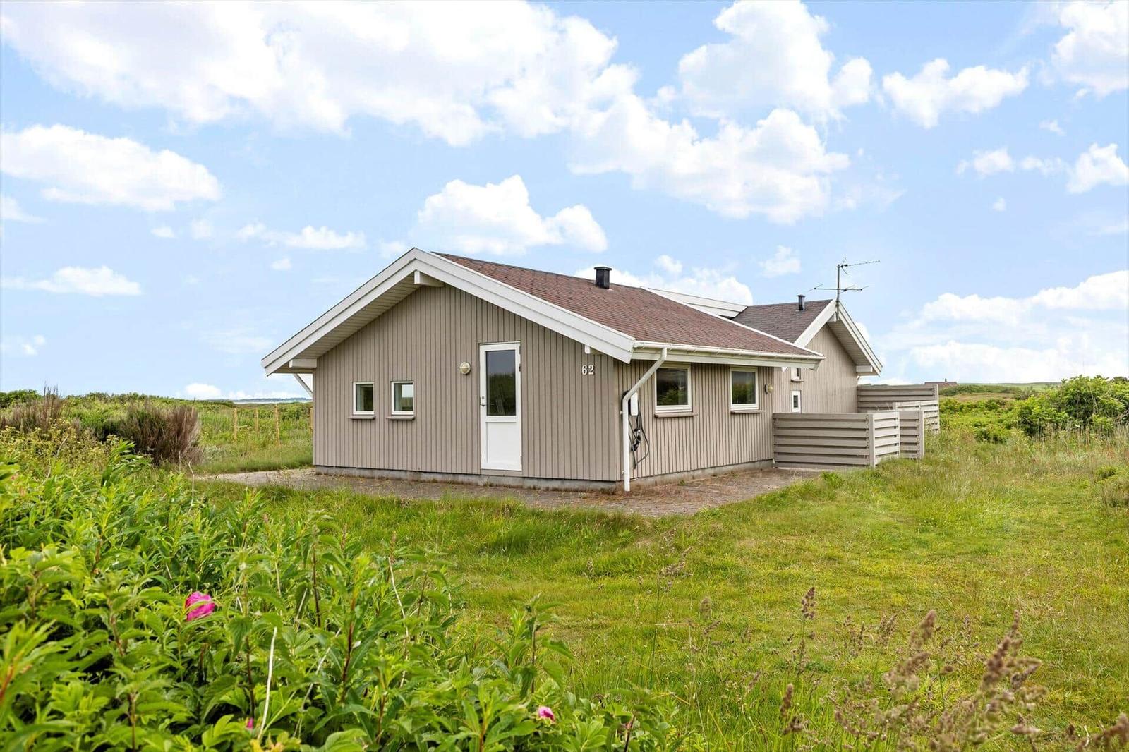 Ein kleines Haus mit grauer Fassade steht in einer grünen Landschaft unter blauem Himmel.