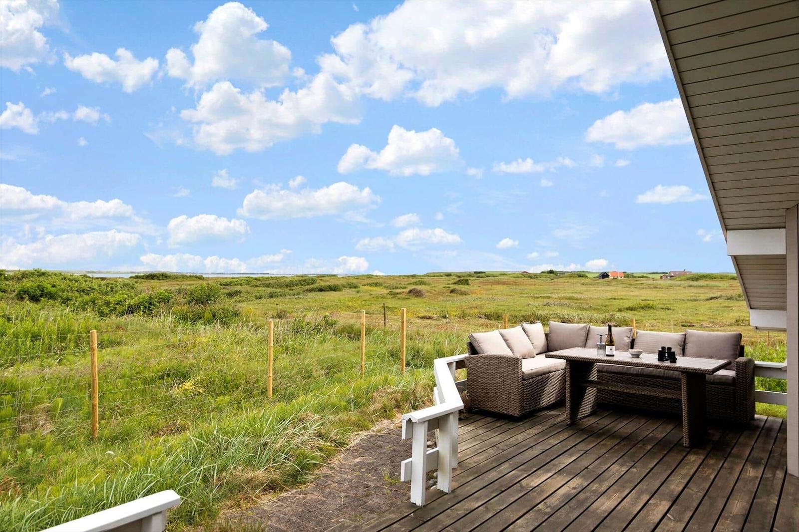 Terrasse mit Sitzgruppe und Tisch, Blick auf grünes Feld und blauen Himmel.