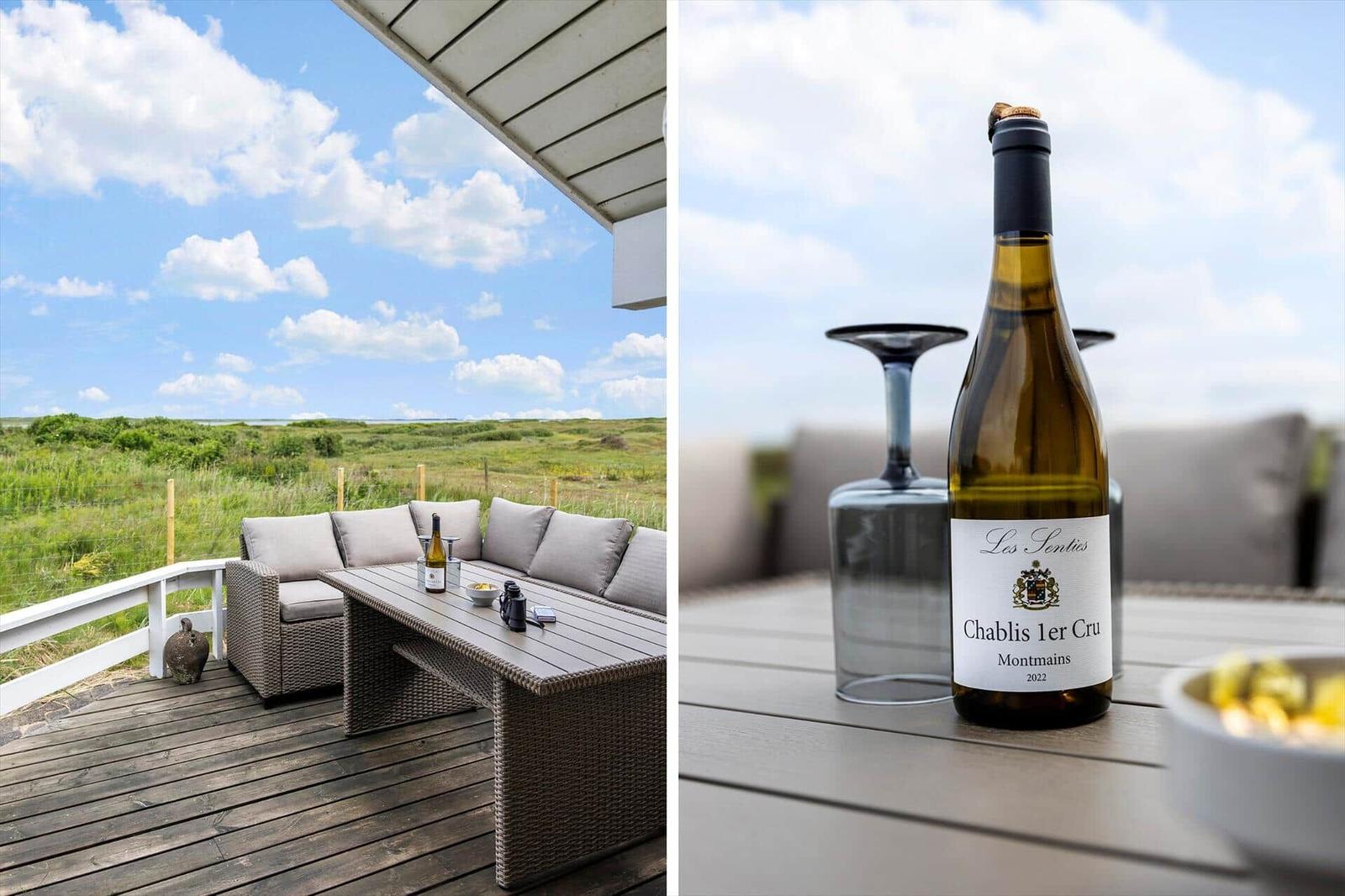 Terrasse mit Sitzgruppe und Weinkrug. Im Hintergrund Grünland unter blauem Himmel.