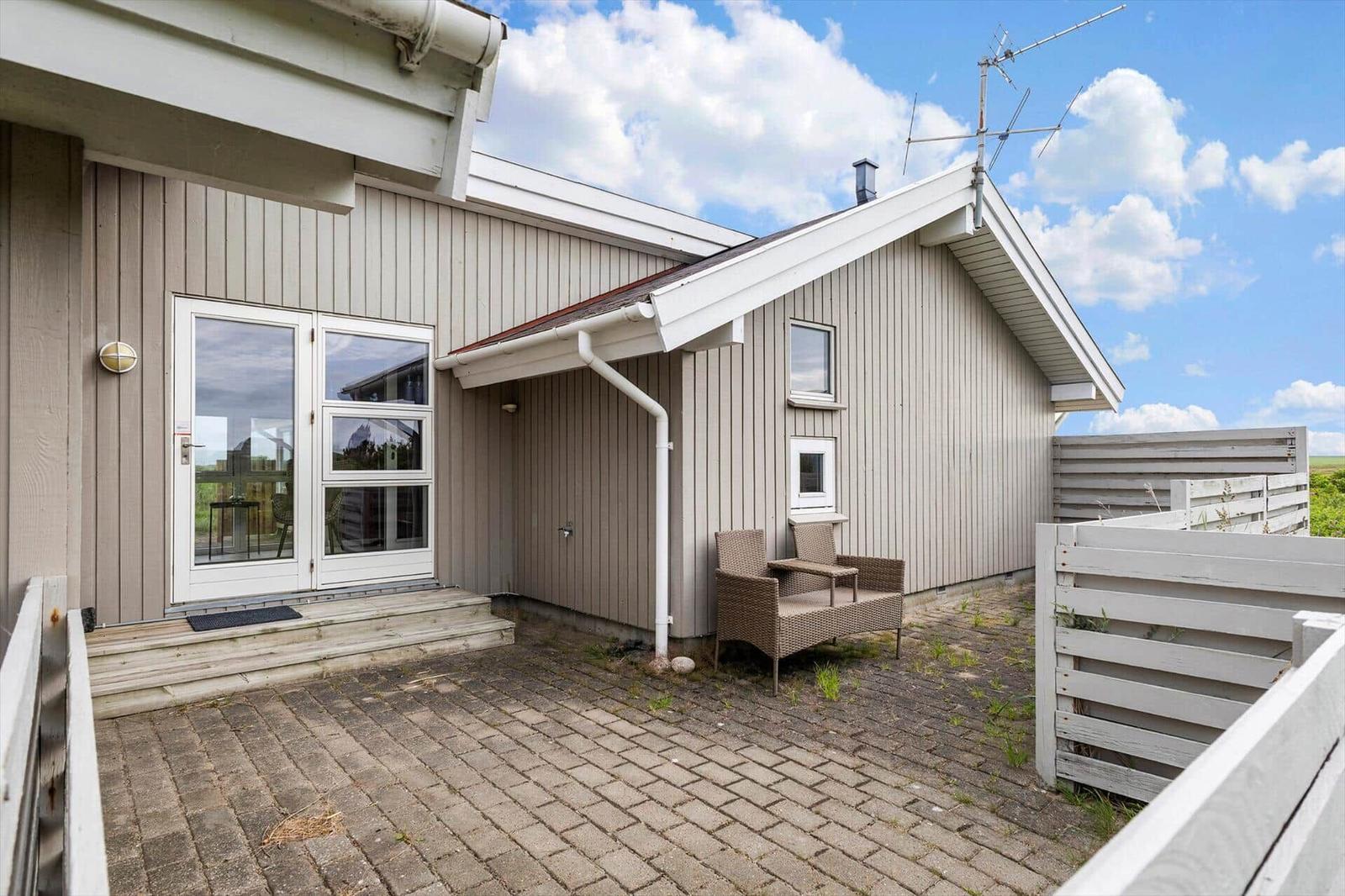 Haus mit Terrasse, Sitzgelegenheit und Gartenzaun unter blauem Himmel.