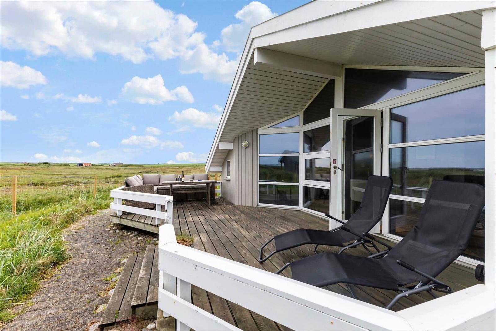 Terrasse mit Liegen und Sitzgruppe, Blick auf Grasland unter blauem Himmel.