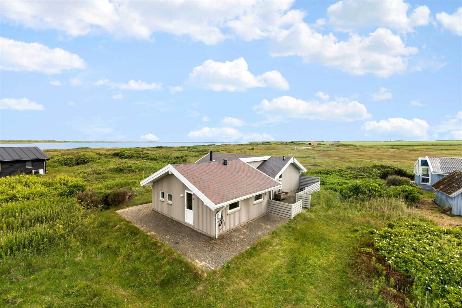 Haus mit Terrasse in grüner Landschaft, See im Hintergrund.