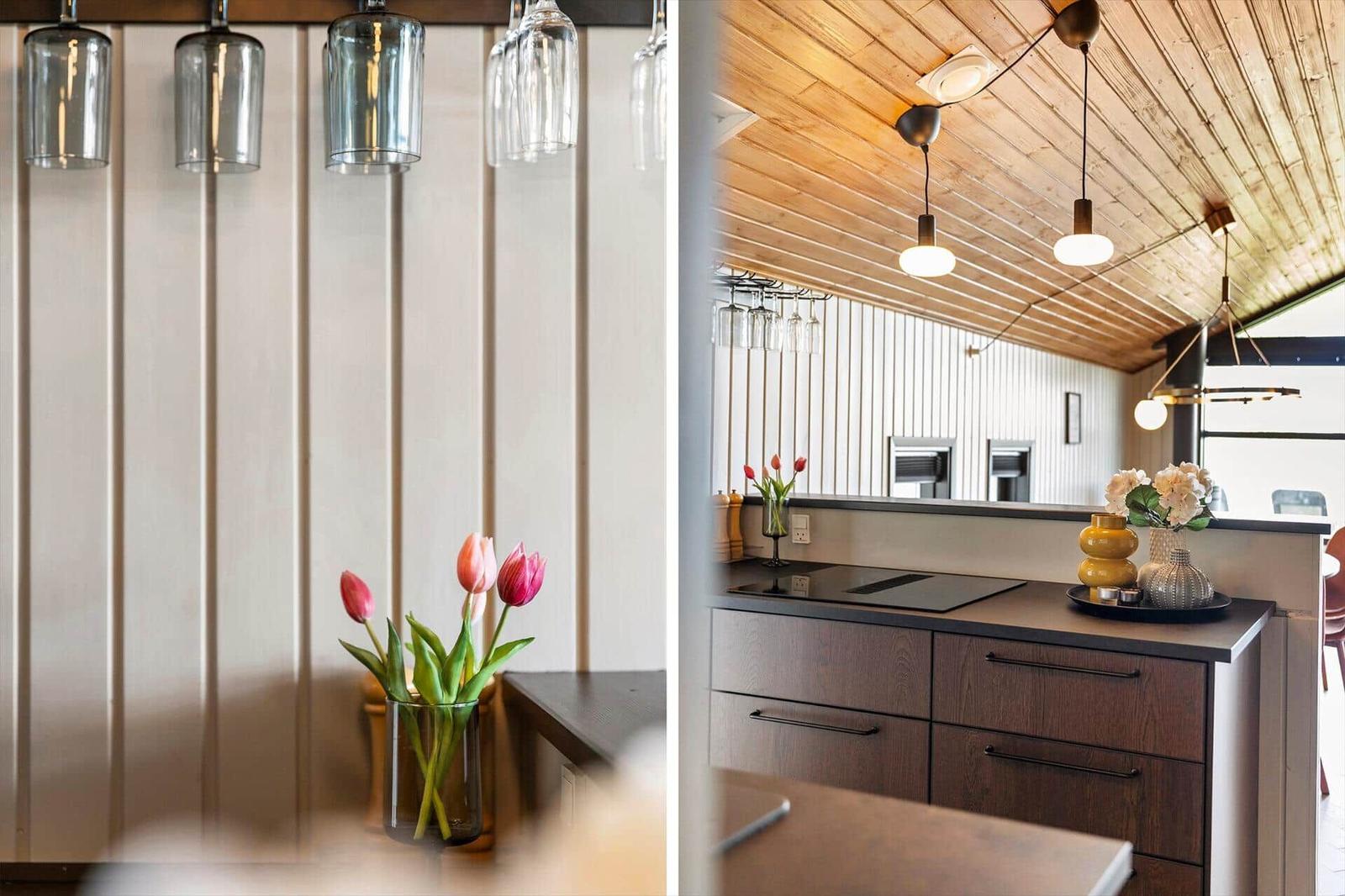 Küche mit Holzdecke, dunklen Schränken und hängenden Glashaltern. Tulpen im Vase auf Arbeitsfläche.